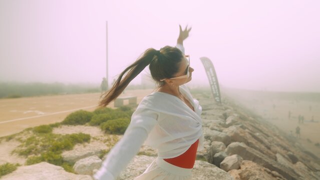 Joyful woman wearing red and white interacts with windy shore