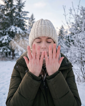 Woman warming her frozen hands with breath winter forest park background cold weather outdoor skincare concept