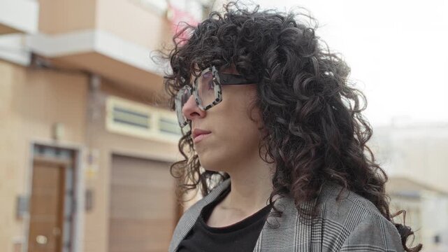 Woman wearing tortoiseshell sunglasses looks sideways on an urban street in front of a building garage door; quiet contemplation.