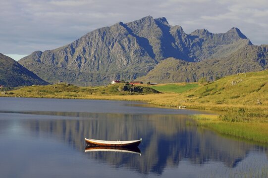 A small wooden boat floats on a calm lake with majestic mountains in the background, Leknes, Vestv&aring;g&oslash;ya, Lofoten, Nordland, Norway
