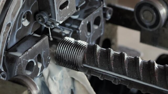 Threaded steel rebar being cut by industrial machine in slow motion
