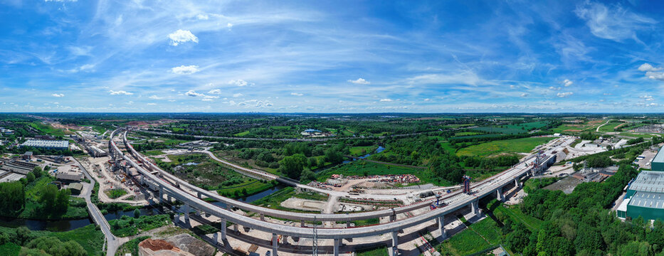 Aerial view of the HS2 Project construction site featuring concrete viaduct pillars and heavy machinery under a bright blue sky in Coleshill, England, United Kingdom.