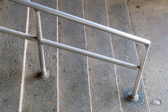Close up high angle view of weathered outdoor concrete stairs and steps featuring a simple grey metal pipe handrail bolted to the ground for pedestrian safety and accessibility in an urban public spac