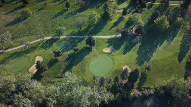 High altitude spring morning drone shot of a fairway at Warm Springs Golf Course, Boise, Idaho. A golf cart drives along the cart path with a sand trap visible and green fairways.