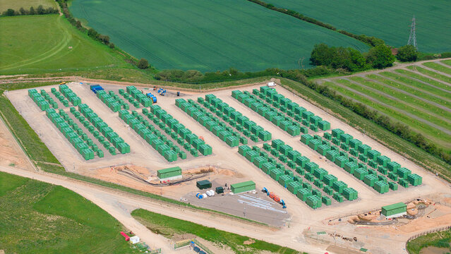 Aerial view of Battery Energy Storage Systems facility with rows of green containers situated among vast agricultural fields and power lines Coleshill, England, United Kingdom.