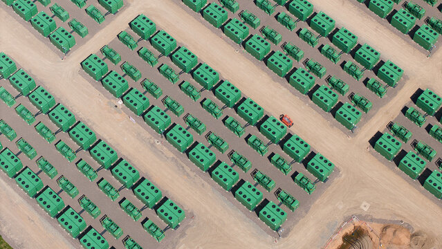 Aerial view of Battery Energy Storage Systems arranged in neat rows on a gravel site under bright sunlight Coleshill, England, United Kingdom.