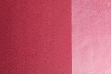 Fototapeta premium A textured wall surface painted in contrasting shades of dark and light pink divided by a vertical line, abstract background, minimalist design, vibrant color contrast.