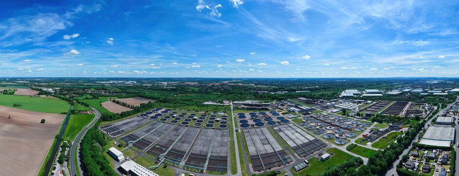 Aerial view of the Severn Trent Water Minworth treatment plant featuring circular tanks and rectangular basins under a blue sky in Birmingham, England, United Kingdom.