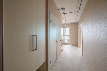 Fototapeta premium light beige hallway with built-in wardrobe, white doors, textured walls, tiled floor, and exposed ceiling wiring in a minimalist style.
