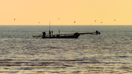 Fototapeta premium Traditional Thai fisherman working on a wooden longtail boat at golden hour.