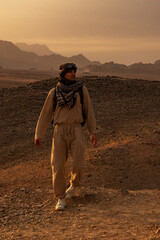 Hurghada Egypt desert tourist man in traditional arabian keffiyeh scarf near mountains at sunset.
