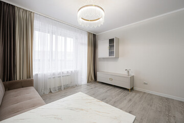 Fototapeta premium light-filled living room with beige tufted sofa, white marble table, elegant circular chandelier, layered curtains, and minimalist white storage unit on grey laminate flooring