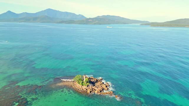 A quiet sea view. A rocky outcrop with a lighthouse at the backdrop of a serene blue sea at dawn