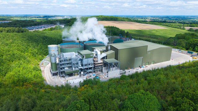 Aerial view of the Biogen Atherstone anaerobic digestion plant with industrial tanks and steam rising, surrounded by lush green woodland in Atherstone, England, United Kingdom.