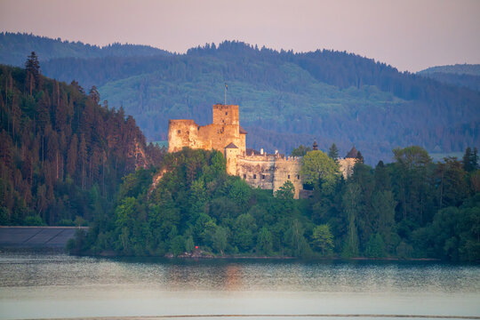 Niedzica Castle, nestled on Lake Czorsztyn amidst forested hills and illuminated by the gentle setting sun, lies on the Velo Czorsztyn cycling route.