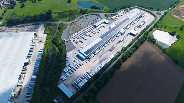 Aerial view of a large industrial distribution center with rows of white semi-trailers parked at loading docks surrounded by green fields Hinckley, England, United Kingdom.