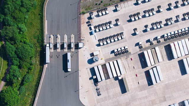 Aerial view of a large logistics distribution center with rows of parked semi-trucks and trailers near a security entrance gate in Hinckley, England, United Kingdom.