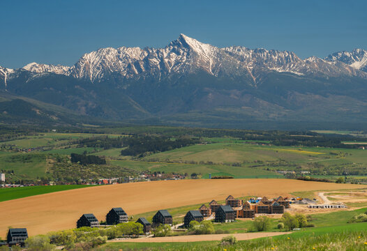 Aerial view of the Demanovska Dolina resort area with modern architecture and green fields under the snow-capped Krivan peak in Demanovska Dolina, Zilina Region, Slovakia.