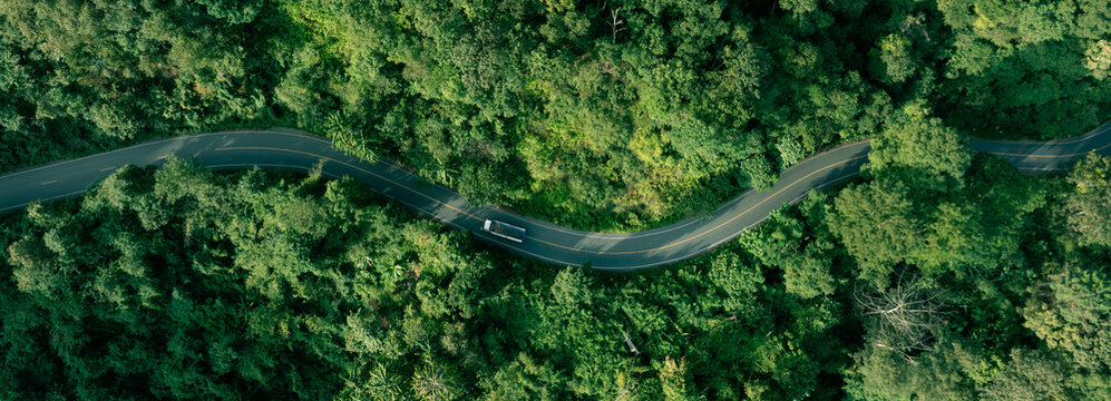 Aerial forest landscape with winding road and vehicles traveling through nature. Concept for sustainable mobility, ESG investment, climate awareness, green transport and eco friendly development.