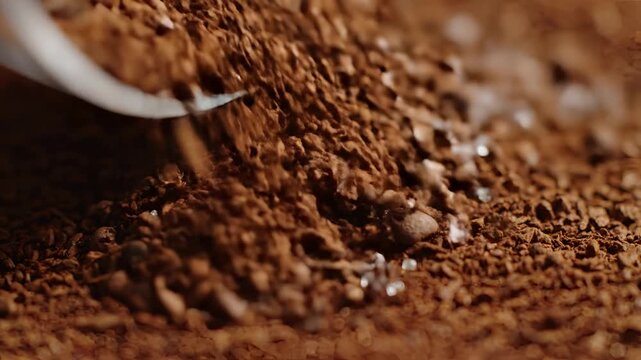 Closeup of coffee beans being poured onto a pile of coffee grounds.