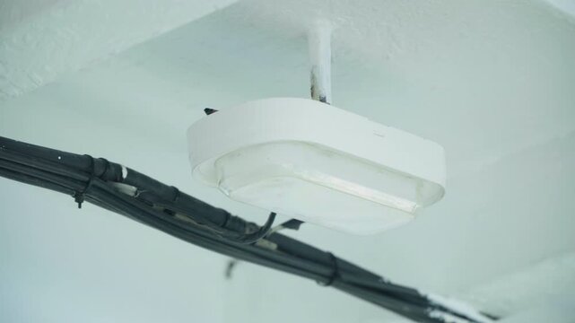 White ceiling light fixture with cables, soft cool light, industrial conduit and plastic casing, closeup of connector and bracket, minimal interior corridor ambience for maintenance inspection