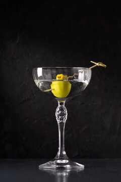 Dry martini with green olive in cocktail glass over white background with reflection. Luxury alcohol drink on bar counter.