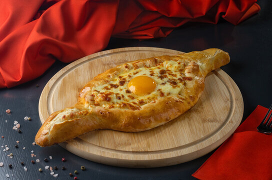 Adjarian khachapuri adorned with mushrooms and a bright egg yolk, served on a rustic wood backdrop.