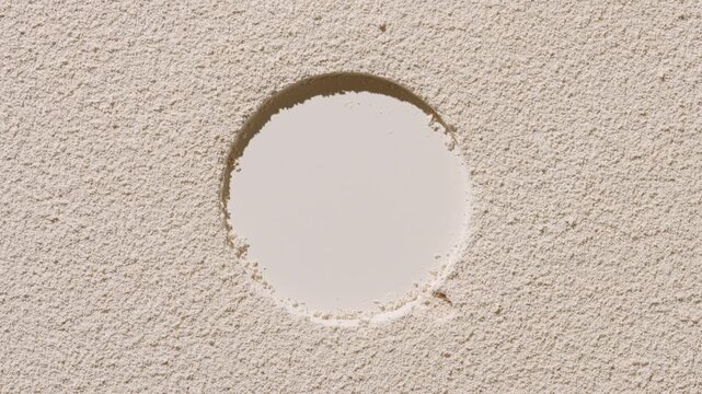 From above shot of beige powder surface with a sifted finish and stamped circular mark lit by rotating light source producing dynamic shadows