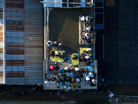 Aerial view of people gathered for Eid Al-Adha prayer on a rooftop in Garung with prayer mats and corrugated metal roofs Kecamatan Kalikajar, Jawa Tengah, Indonesia.