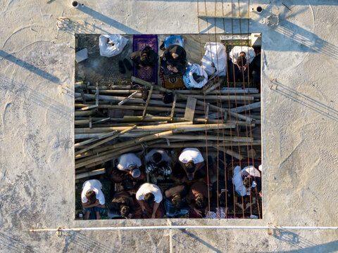 Aerial view of people performing Eid Al-Adha prayer inside a square concrete opening with bamboo poles and rebar in Kecamatan Kalikajar, Jawa Tengah, Indonesia.