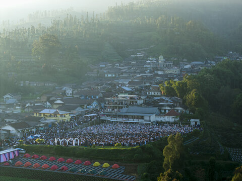 Aerial view of a large crowd gathered for Eid Al-Adha prayer in Garung village surrounded by misty mountains and lush greenery in Kecamatan Kalikajar, Jawa Tengah, Indonesia.