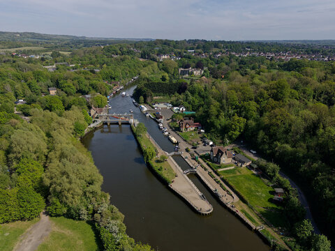 Allington lock on the river Medway. Aerial view of built structure on the river regulating water levels. Boats sailing and mooring. High altitude panoramic view of green landscape in Kent, UK.
