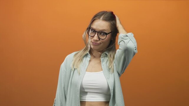 Woman with glasses touches her head and tucks hair behind ear while revealing midriff in studio; confusion contemplation.