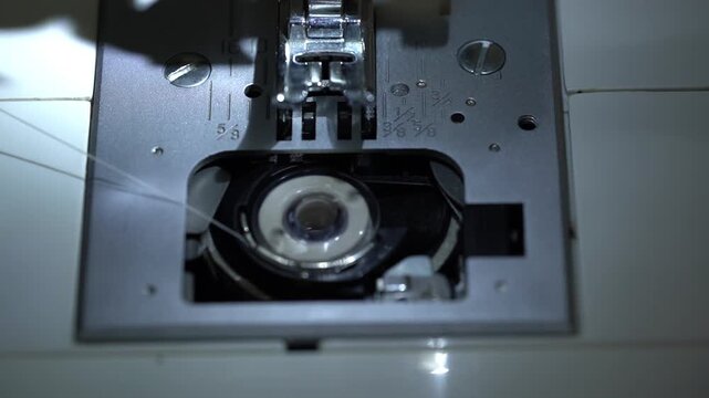 Close-up of a sewing machine bobbin inserted into the shuttle hook mechanism while thread unwinds during