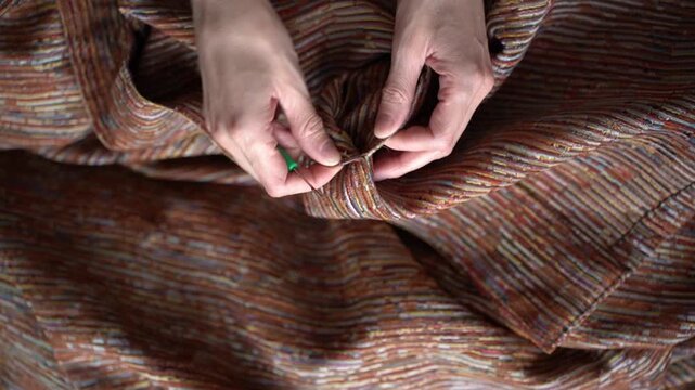 Removing sewing machine stitches with a seam ripper, close-up of hands.