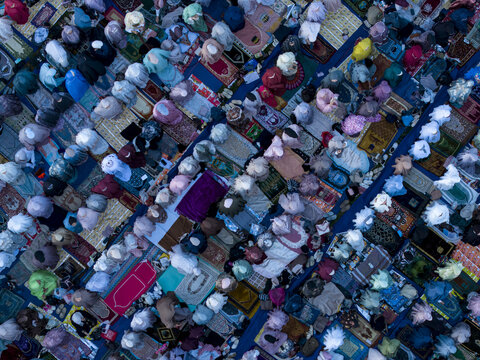Aerial view of a large crowd of Muslim worshippers gathered for Eid Al-Adha prayer on colorful prayer mats in Kecamatan Kalikajar, Jawa Tengah, Indonesia.
