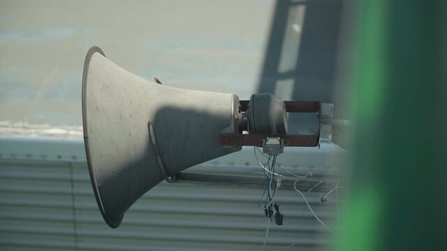 Weathered rooftop speaker dripping water, industrial rooftop mounted horn covered in rust and cobwebs, water droplets falling from mounting bracket, soft morning light casting long shadows, muted