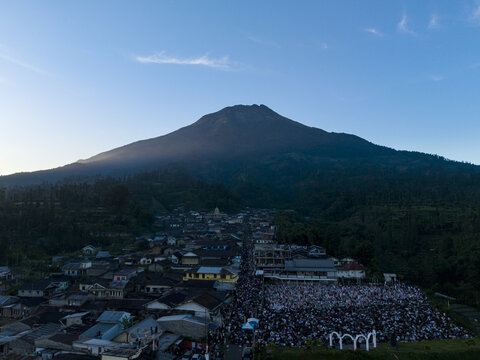 Aerial view of a large crowd gathered for Eid Al-Adha prayer in a village at the foot of Mount Sumbing under a clear blue sky Kecamatan Kalikajar, Jawa Tengah, Indonesia.