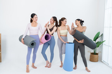 Naklejka premium Asian women friends hold colorful yoga mats and share high five in bright studio, fitness community celebrates teamwork, wellness motivation, flexibility progress, posture balance, healthy habit