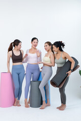 Obraz premium Asian female friends stand with yoga mats, smiling and talking after wellness class, sharing body confidence, fitness motivation, community support, healthy lifestyle routine on clean studio backdrop.