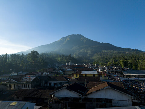 Aerial view of a large crowd gathered for Eid Al-Adha prayer in a village at the foot of Mount Sumbing under a clear blue sky in Kecamatan Kalikajar, Jawa Tengah, Indonesia.