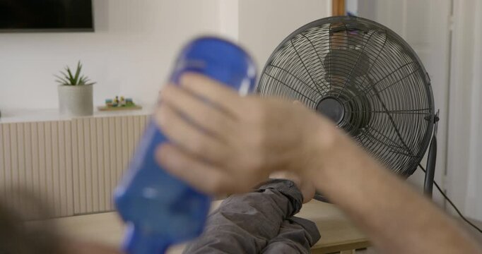 Beat the Heat: A person's hand holds a blue bottle, seemingly attempting to cool down in front of a rotating fan. The scene suggests a hot day and the common struggle for relief.
