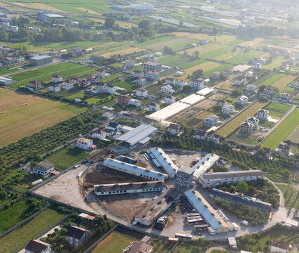 Aerial view of an industrial complex with a star-shaped layout surrounded by residential houses and green agricultural fields in Tirana County, Albania.