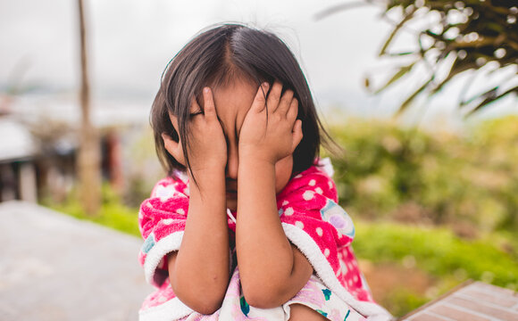 Ni&ntilde;a cubriendo su rostro con las manos al aire libre en expresi&oacute;n de timidez o emoci&oacute;n