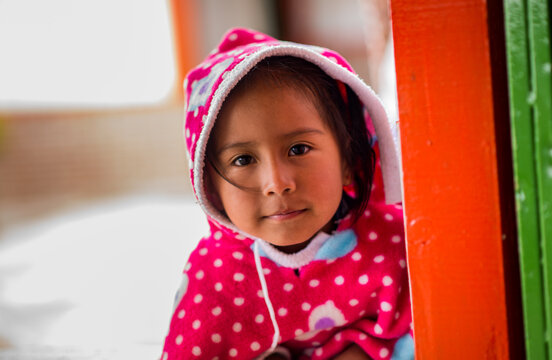 Ni&ntilde;a sonriente con manta rosa de lunares y capucha mirando a c&aacute;mara en entorno hogare&ntilde;o