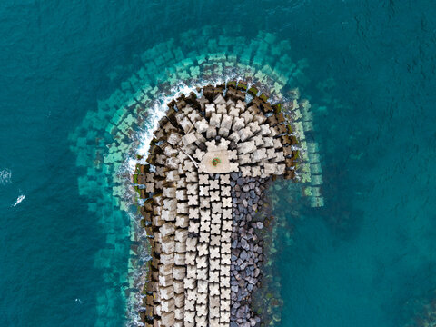Aerial view of the Porta do Povoamento breakwater featuring concrete tetrapods and clear blue water in Povoacao, Acores, Portugal.