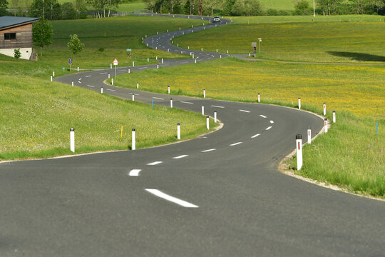 Empty winding road through green spring meadows in the rural countryside of Styria, Austria