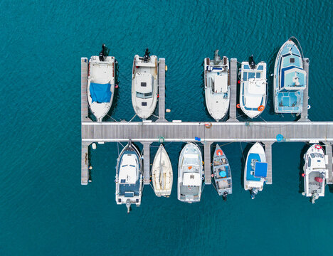 Aerial view of boats moored at a wooden pier in clear turquoise water at the marina in Povoacao, Acores, Portugal.