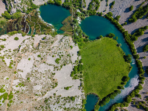 Aerial view of Kudin most na Krupi spanning the turquoise Krupa river with cascading waterfalls and lush green meadows in Golubic, Zadarska zupanija, Croatia.