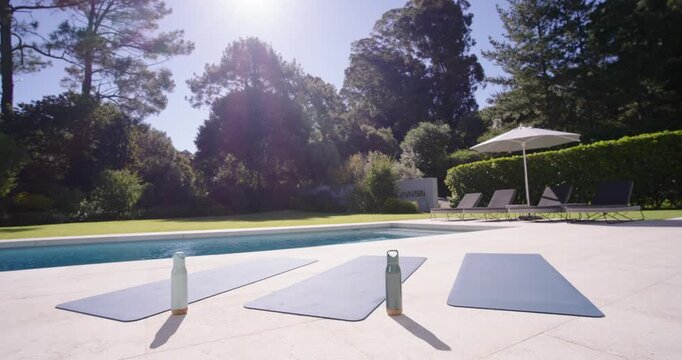 Camera pulling back is revealing two water bottles appearing upright on blue mats by pool